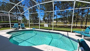 Une piscine dotée d’une enceinte en verre, entourée de chaises longues et offrant une vue sur les arbres et les maisons.
