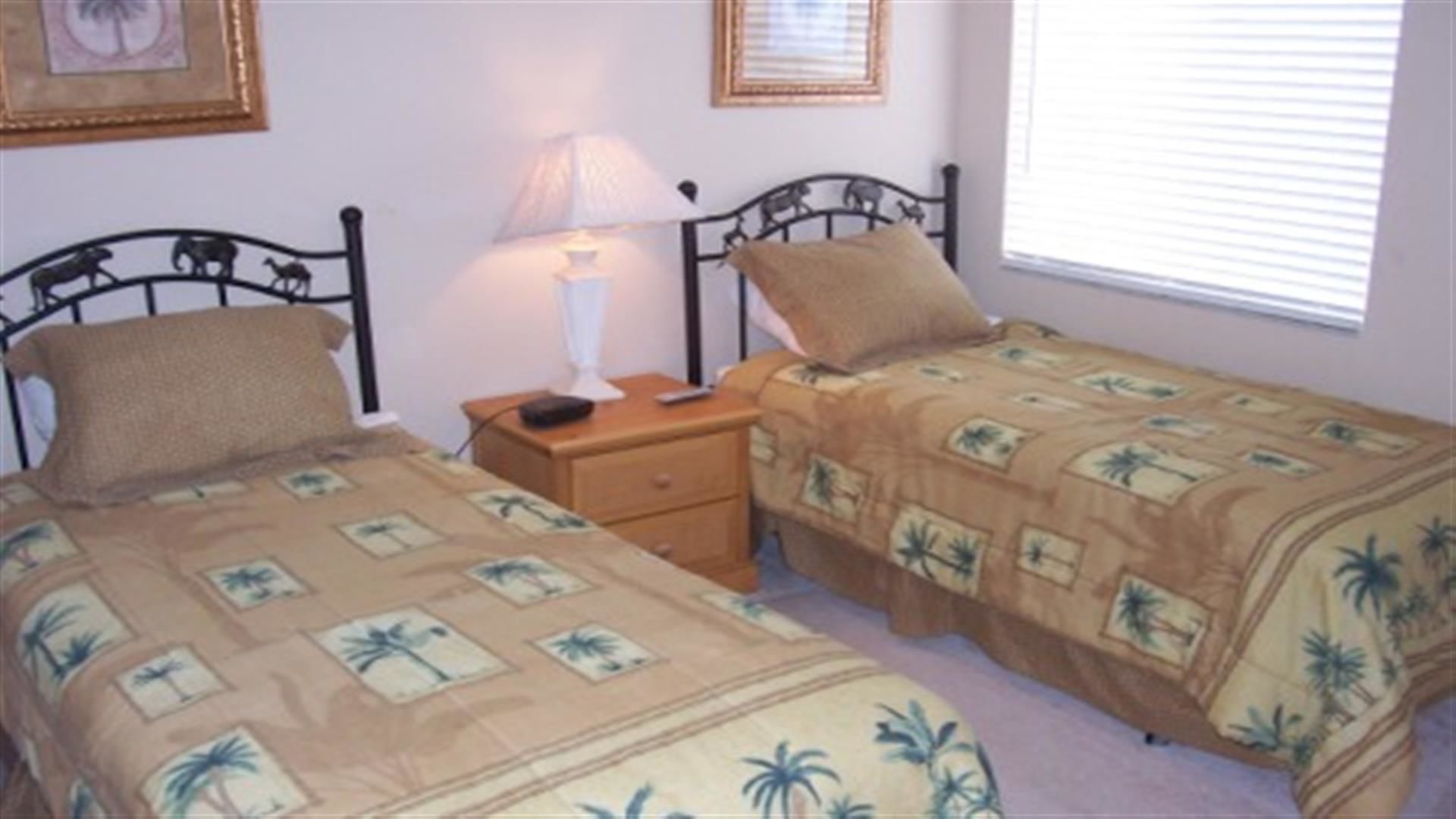 Une chambre avec deux lits simples, une table de chevet avec une lampe et une fenêtre avec des stores.