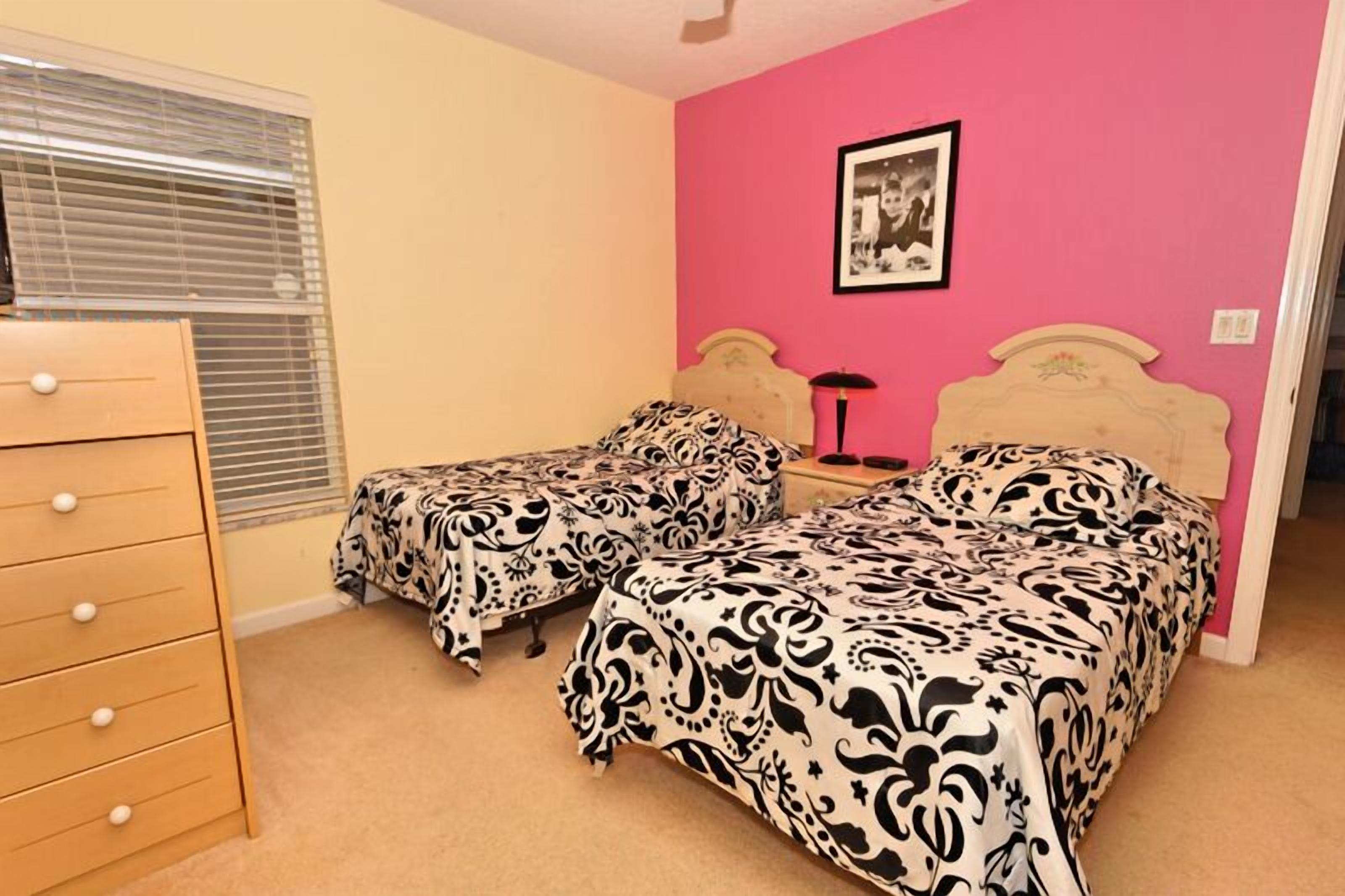 A bedroom with two beds, a dresser, and a framed picture on the wall.