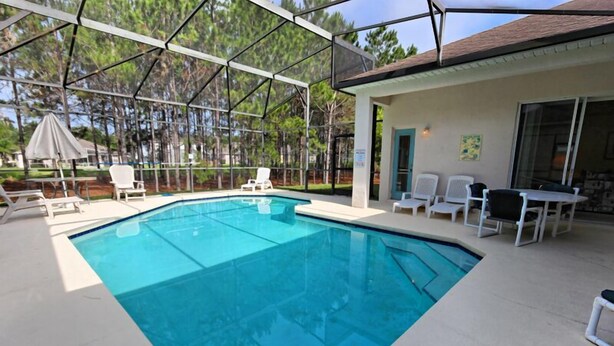 A swimming pool with a covered patio area, outdoor chairs, and a building with a door and windows.