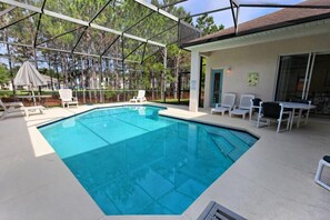 A swimming pool with a covered patio area, outdoor chairs, and a building with a door and windows. - Ov3156 - Highlands Reserve - 4 Bed 3 Baths Villa (Davenport)