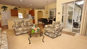 A living room with two patterned sofas, a coffee table, and a dining area with a table and chairs.