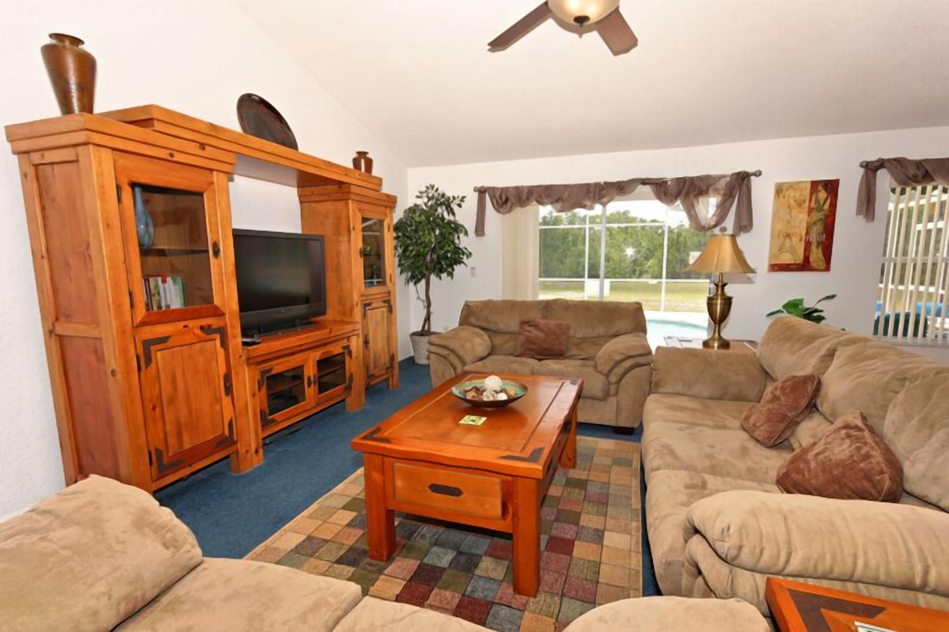 A living room with a wooden entertainment center, a television, a sofa, a coffee table, and a ceiling fan.