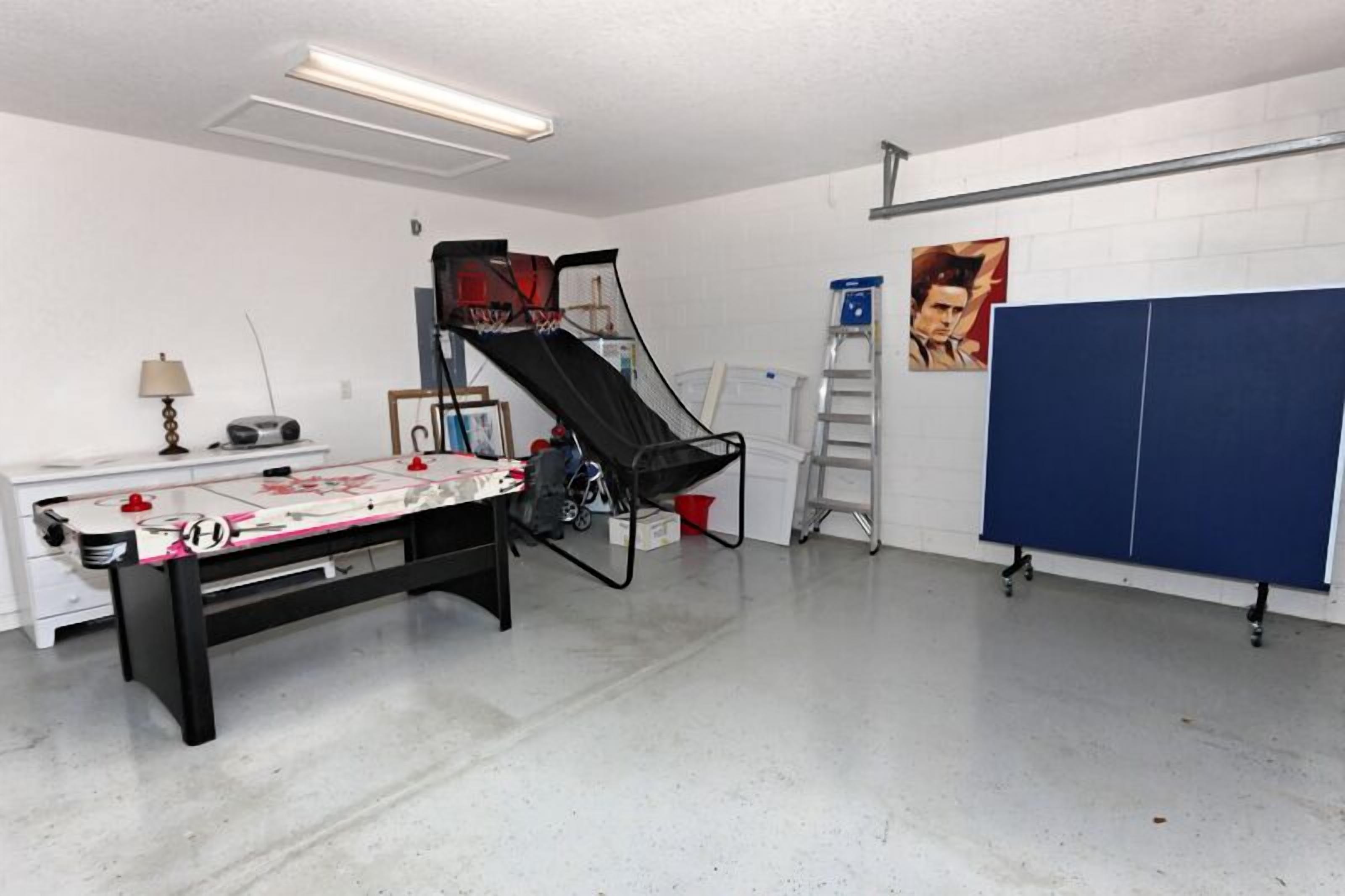 A room with a foosball table, a ping pong table, and a basketball hoop.
