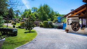 A rural setting with a gravel driveway leading to a wooden building with a large wheel feature. - Moulin des Sandaux Natur'park (Saint-Andre-et-Appelles)