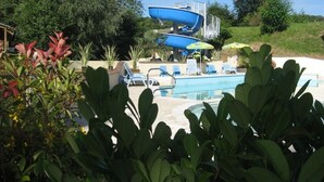 A pool area with a water slide, lounge chairs, and a small building. - Moulin des Sandaux Natur'park (Saint-Andre-et-Appelles)
