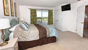 A bedroom with a bed, a nightstand, a TV mounted on the wall, and a window with curtains.