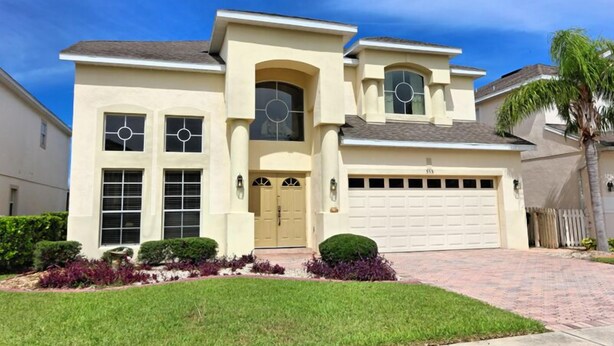A two-story house with a beige facade, a garage, and a well-maintained lawn.