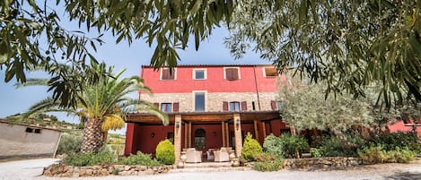 A two-story building with a red facade, a stone foundation, and a covered patio with outdoor furniture.