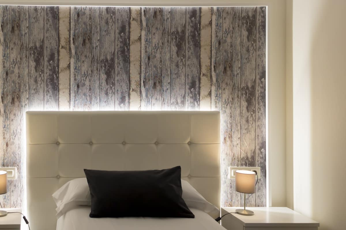 A neatly made bed with a tufted headboard, two bedside lamps, and a wall with a distressed wood panel design.