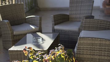 Mueble de mimbre con cojines, una mesa de vidrio y una planta en maceta con hojas variegadas.