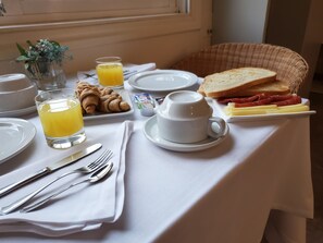 A breakfast table with croissants, cheese, ham, and toast. There are also plates, cutlery, and a glass of orange juice. - Hotel O Pazo (Vigo)