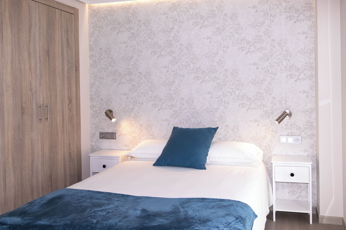 A bedroom with a bed, nightstands, a wardrobe, and a wall with a floral pattern.