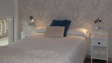A neatly made bed with a fluffy white cover, two bedside tables with lamps, and a patterned wallpaper.