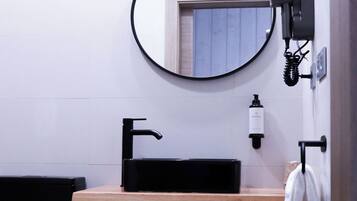 Een badkamer met een zwarte wastafel, een spiegel, een handdoekrek en een prullenbak.