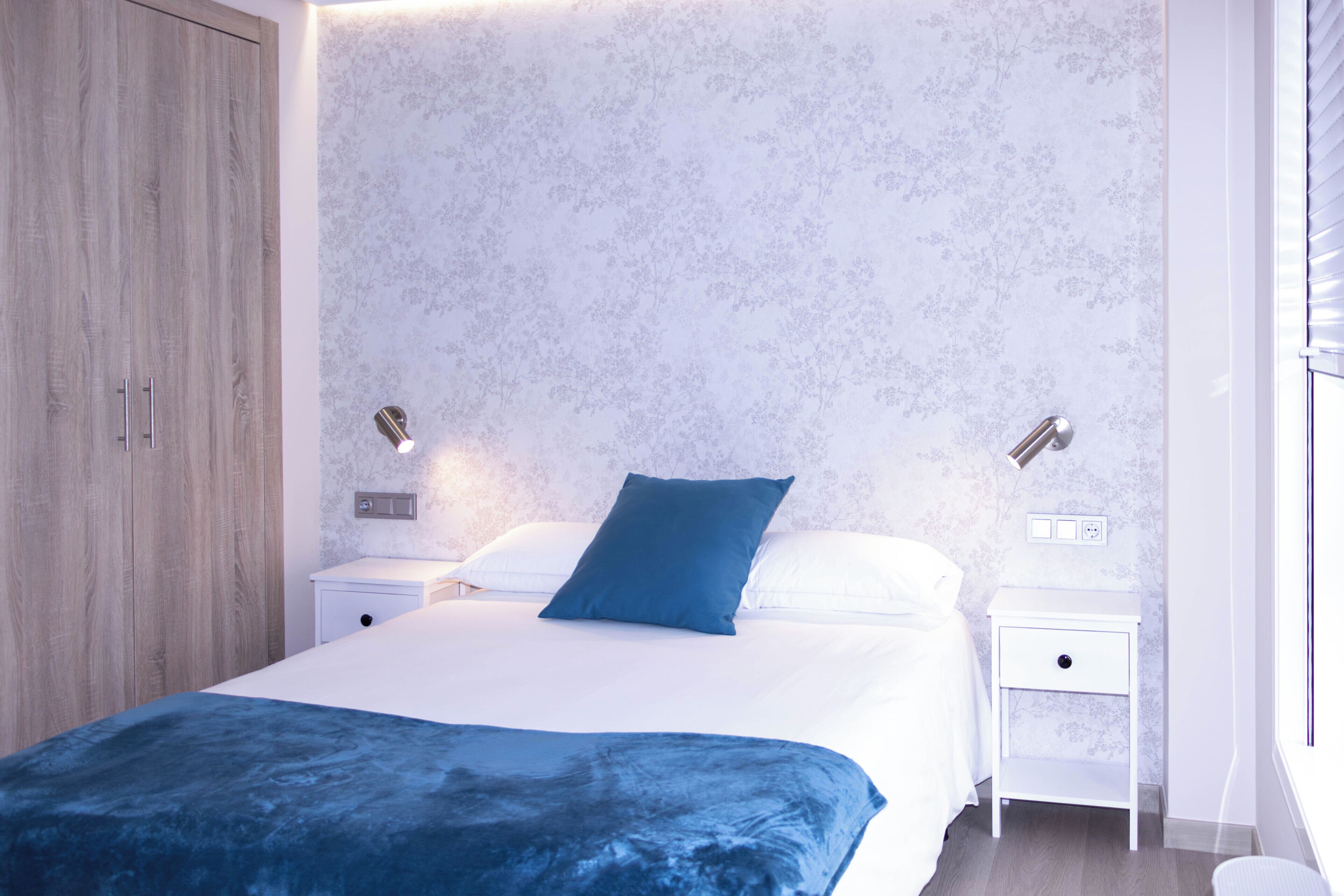 Un dormitorio con cama, mesitas de noche, armario y ventana con persianas.
