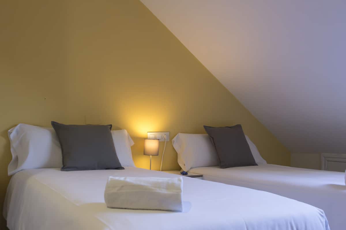 A hotel room with two beds, a nightstand, and a wall-mounted lamp.