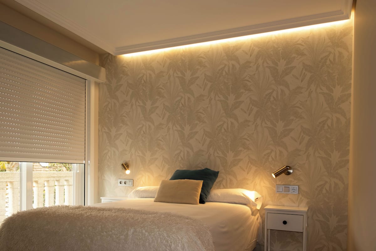 A bedroom with a bed, two bedside lamps, a nightstand, and a window with blinds.