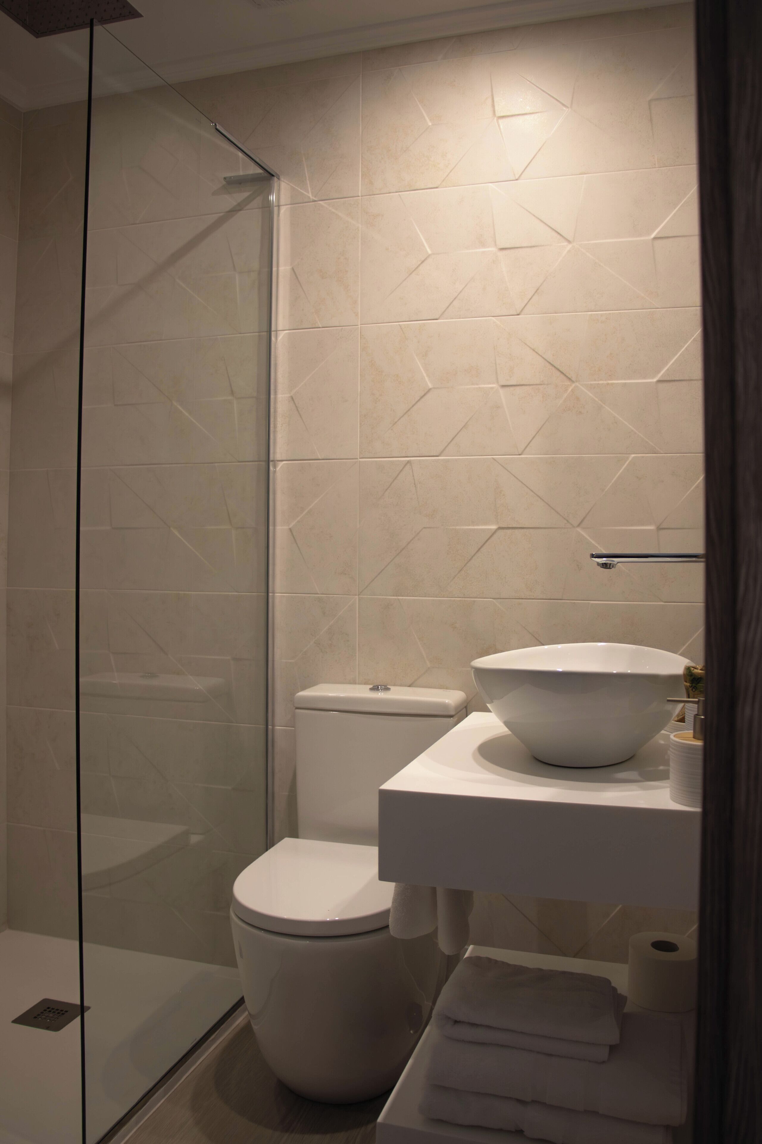 A bathroom with a glass shower enclosure, a toilet, a sink with a large basin, and a towel rack.