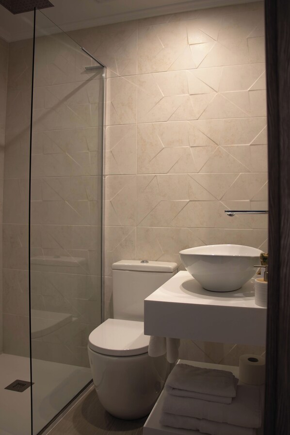Un baño con cabina de ducha de vidrio, inodoro, lavabo de gran tamaño y toallero.