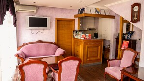 A reception area with a wooden counter, a television, and a clock on the wall. - Guest House Vijecnica (Sarajevo)