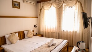A double bed with a quilt, two pillows, a bedside table with a kettle, and a TV on a stand. - Guest House Vijecnica (Sarajevo)