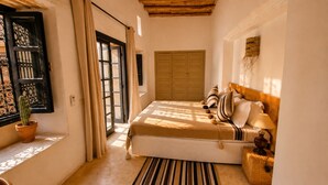 A bedroom with a bed, curtains, a window with a view, a wooden headboard, and a bedside lamp.