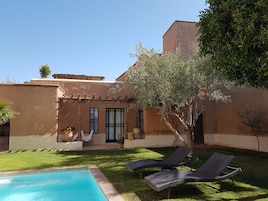 Zona junto a la piscina con sillones de descanso y un pequeño jardín.