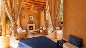 A cozy lounge area with wicker furniture, a fireplace, and a blue rug. - Tagadert Lodge (Tameslouht)