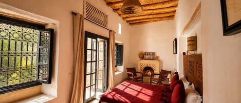 Un dormitorio con una cama grande, una chimenea y una ventana con vistas a follaje.