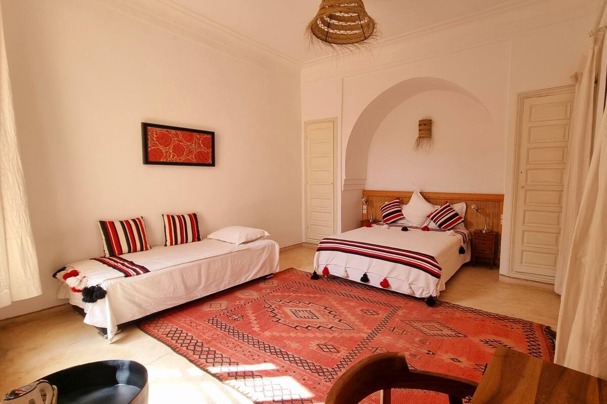 Ein Schlafzimmer mit zwei Betten, einem roten Teppich mit Muster, einem Holzstuhl und einer Hängelampe.