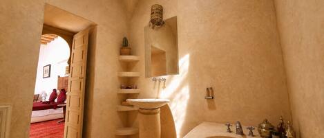A bathroom with a freestanding bathtub, a shelf with toiletries, and a mirror above the sink.