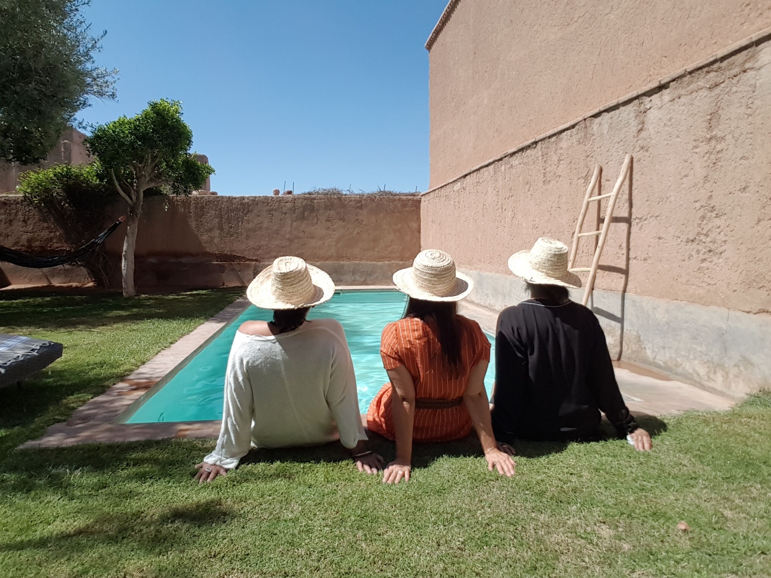 Three people sitting by a pool with a ladder and a hammock in the background.
