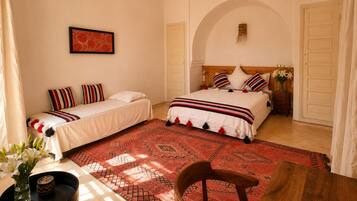 A room with two beds, a dining table, and a red patterned rug.