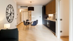 Una cocina moderna con armarios oscuros, un comedor con mesa y sillas redondas, y un reloj de pared grande.