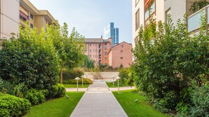 Un sendero conduce a un edificio de diseño moderno, rodeado de follaje cuidado y un cielo despejado.
