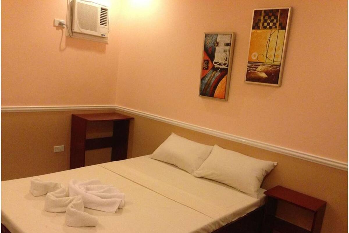Habitación de hotel con cama, mesita de noche, aire acondicionado instalado en la pared y dos cuadros.