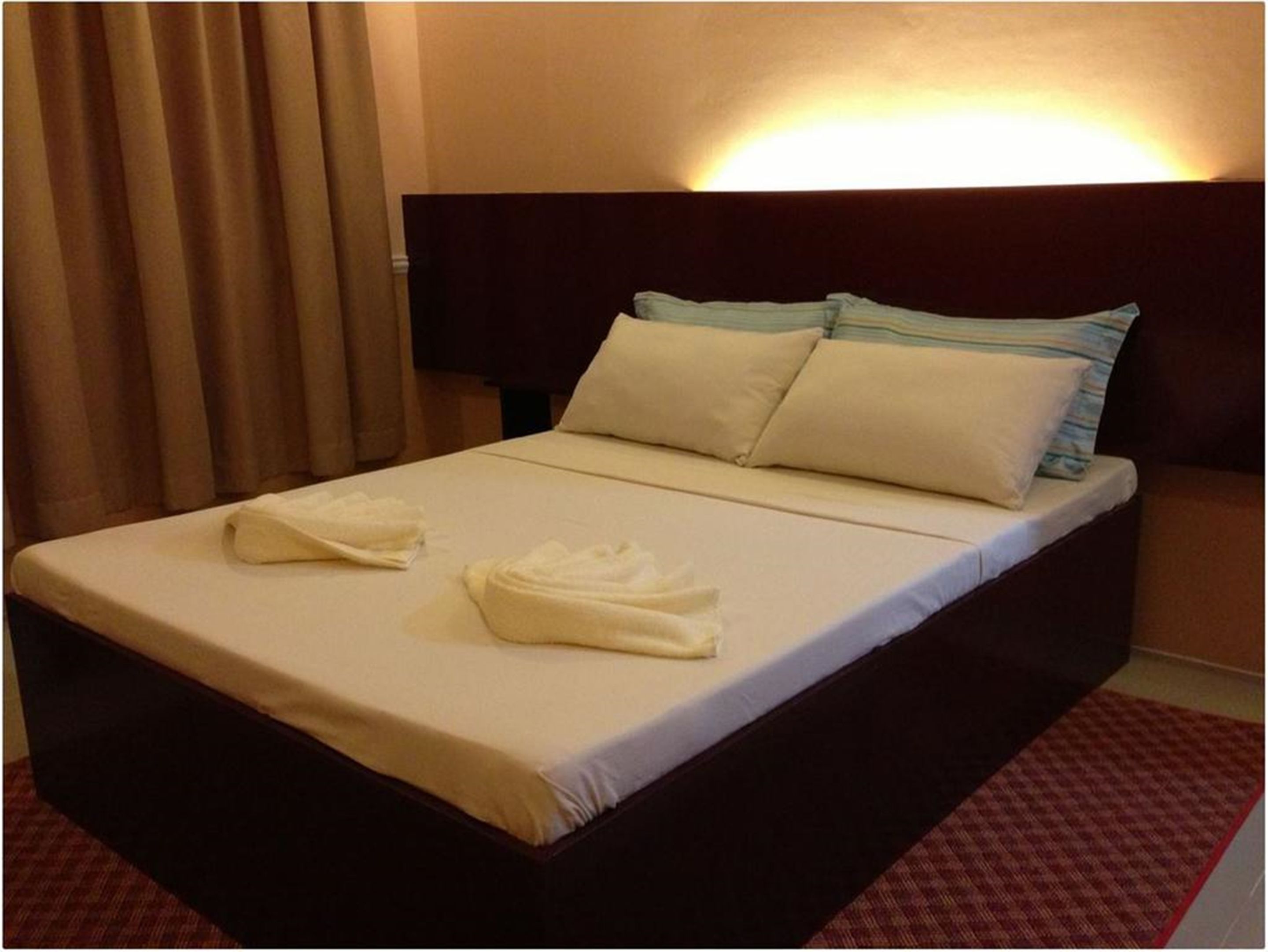Una cama bien hecha con dos toallas, un cabecero oscuro y un suelo cubierto de alfombra roja.
