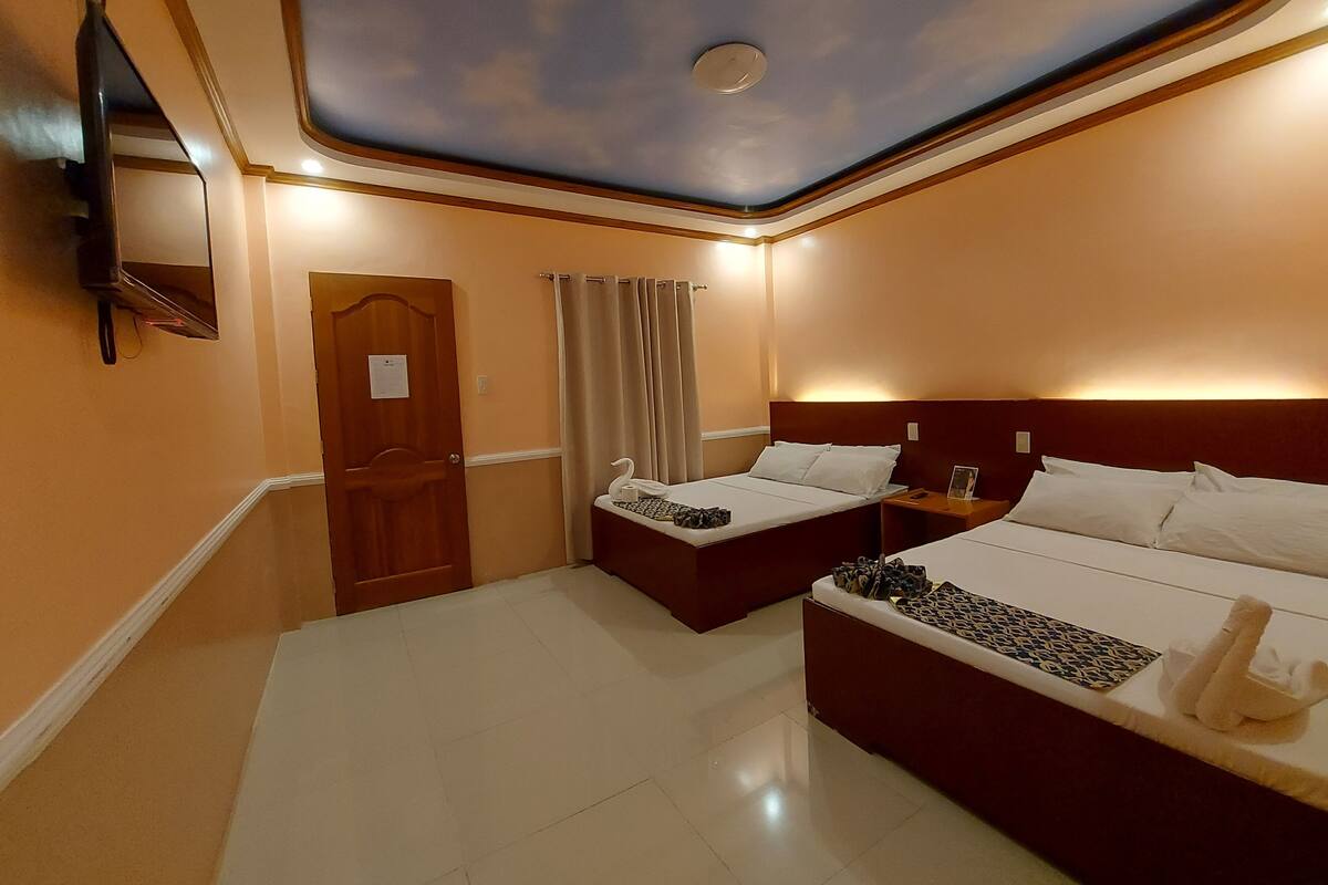 Habitación de hotel con dos camas, techo con diseño de nubes, televisor de pantalla plana y puerta con un letrero.