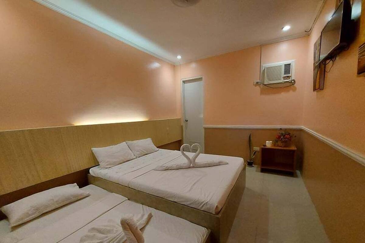 Habitación de hotel con dos camas, una mesita de noche, un armario pequeño, un televisor montado en la pared y un equipo de aire acondicionado.