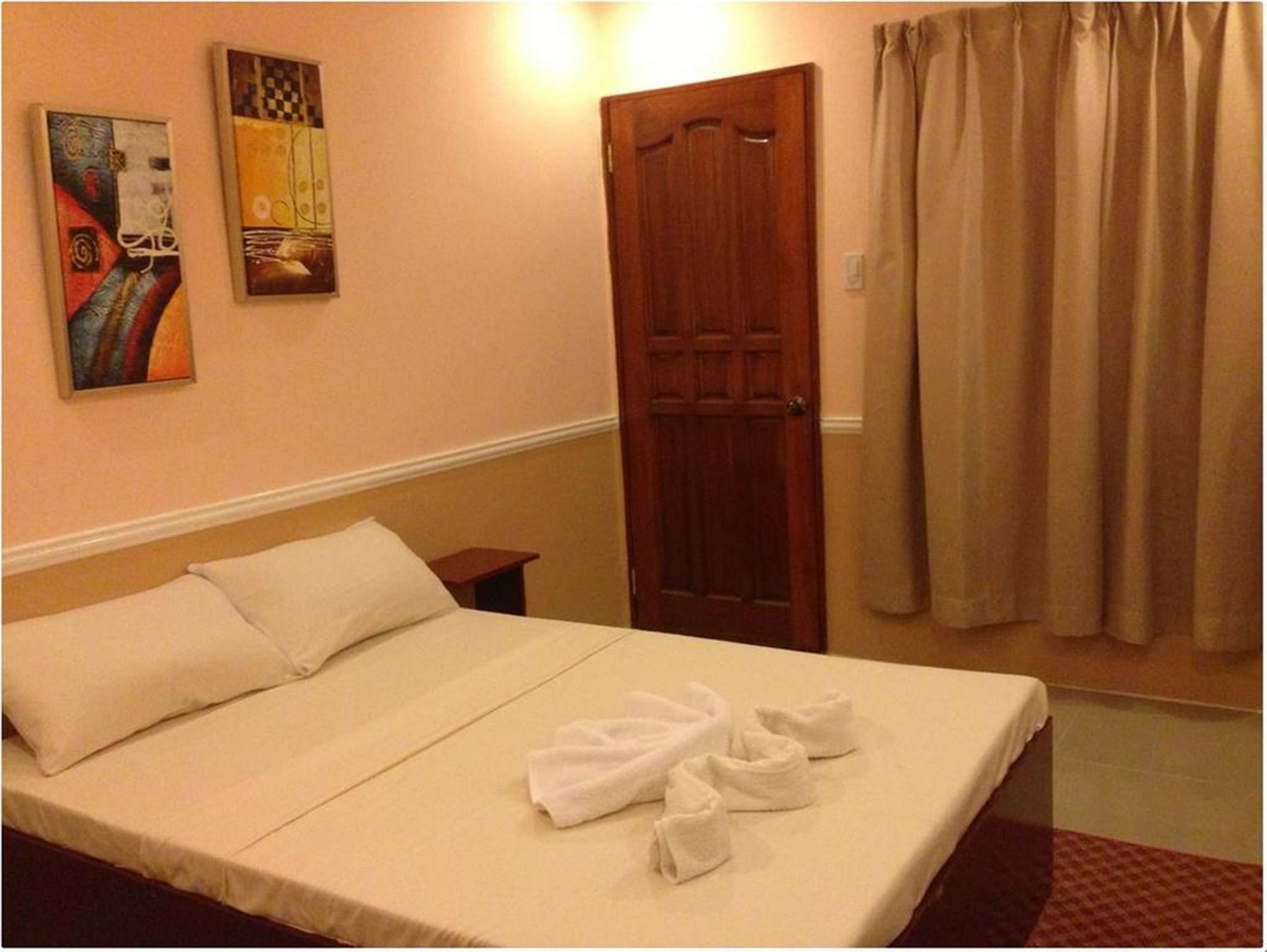 A hotel room with a bed, a wooden door, and two paintings on the wall.