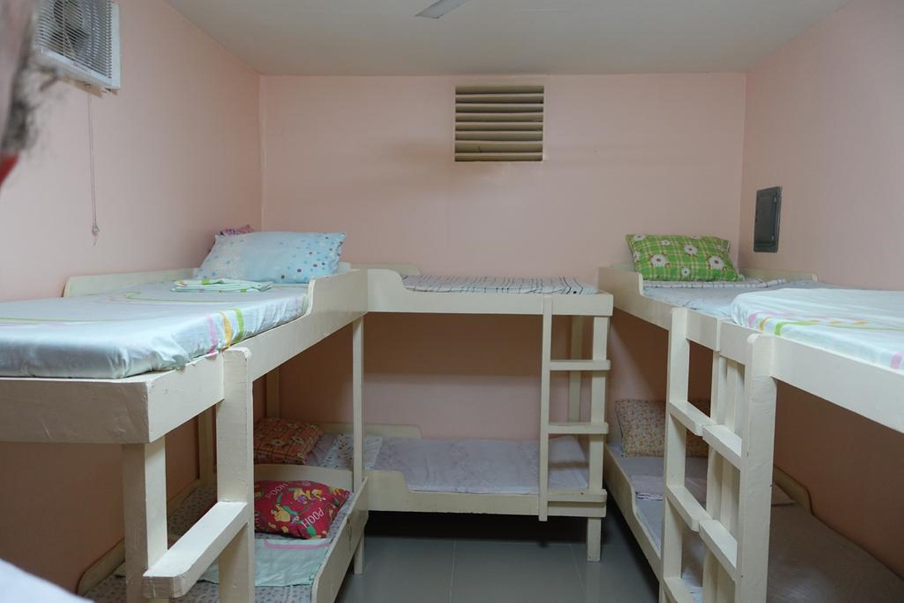 A room with bunk beds, a small window, and a wall-mounted air conditioner.