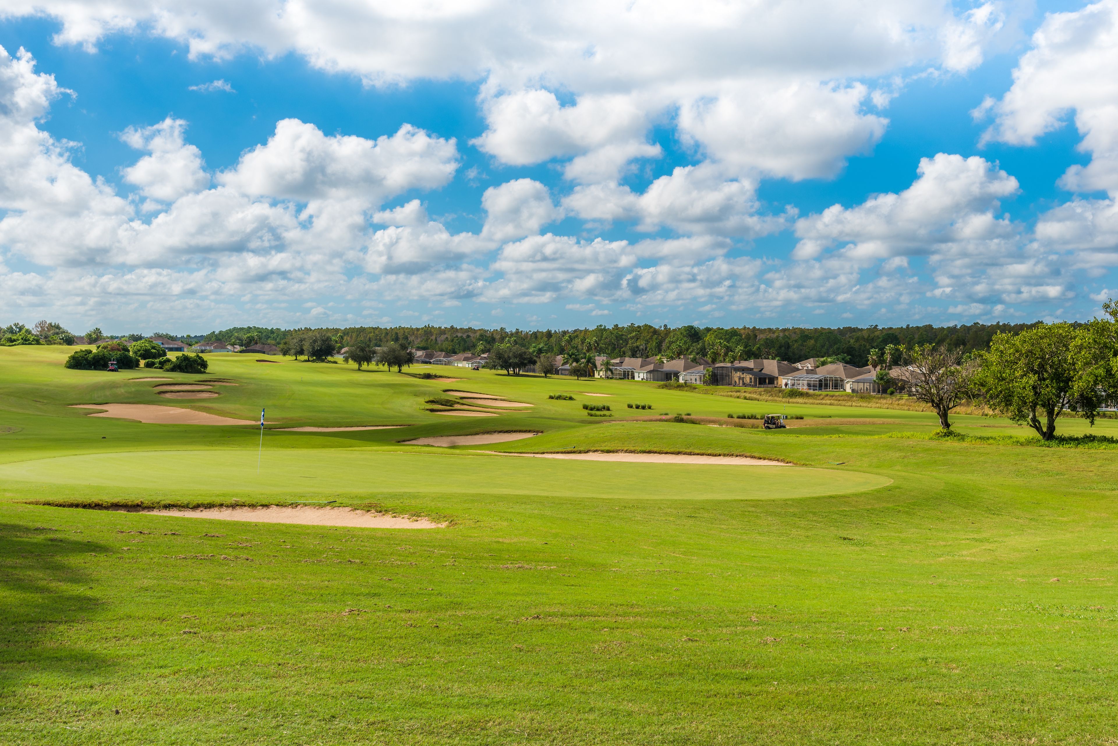 Un parcours de golf avec des bunkers, un mât de drapeau et un ciel bleu dégagé.