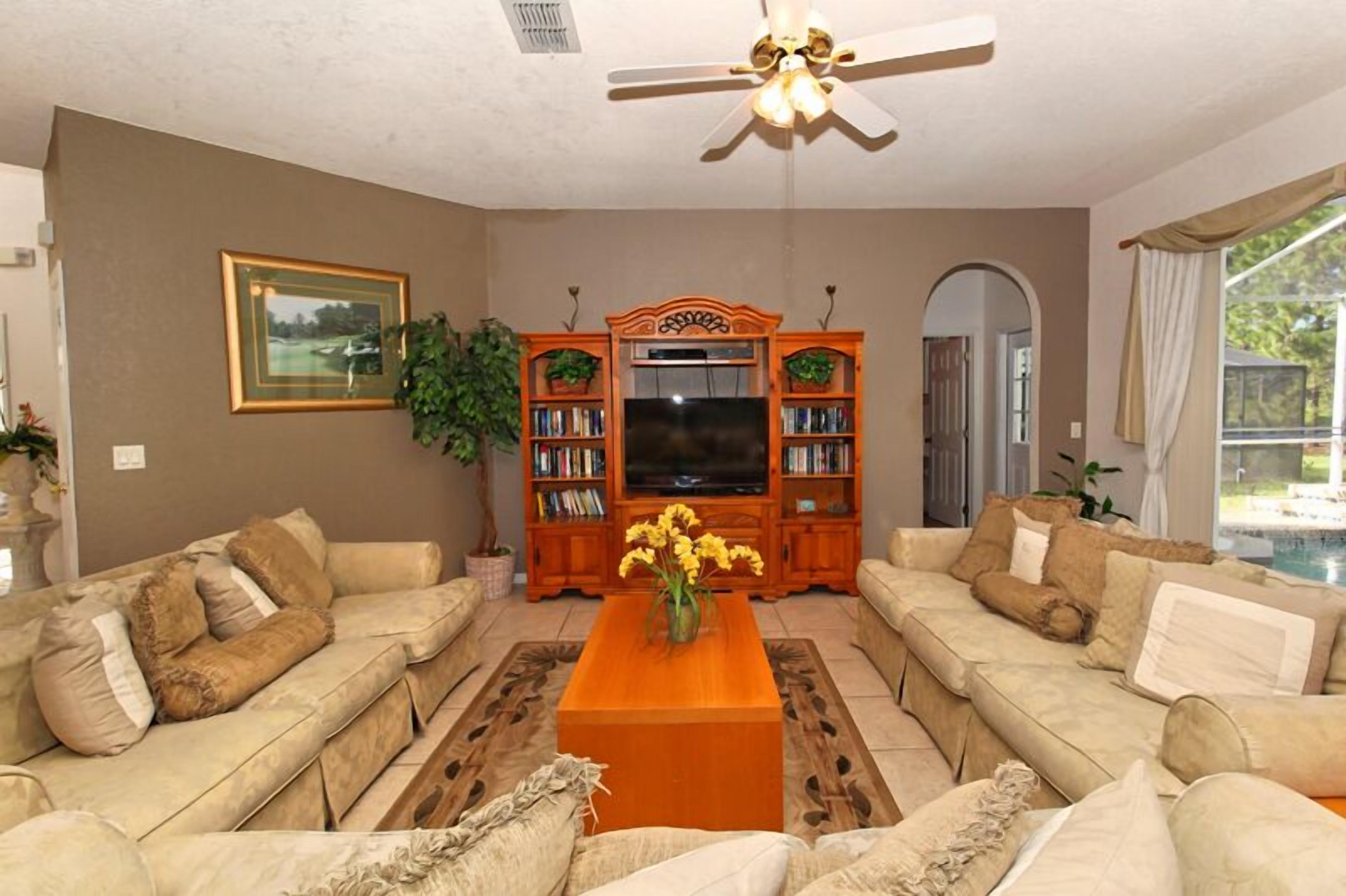 A living room with beige sofas, a wooden coffee table, a television, and bookshelves.