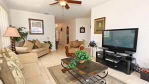 A living room with a sofa, armchair, coffee table, television, and ceiling fan. - Ov3131 - Highlands Reserve - 5 Bed 3 Baths Villa (Davenport)