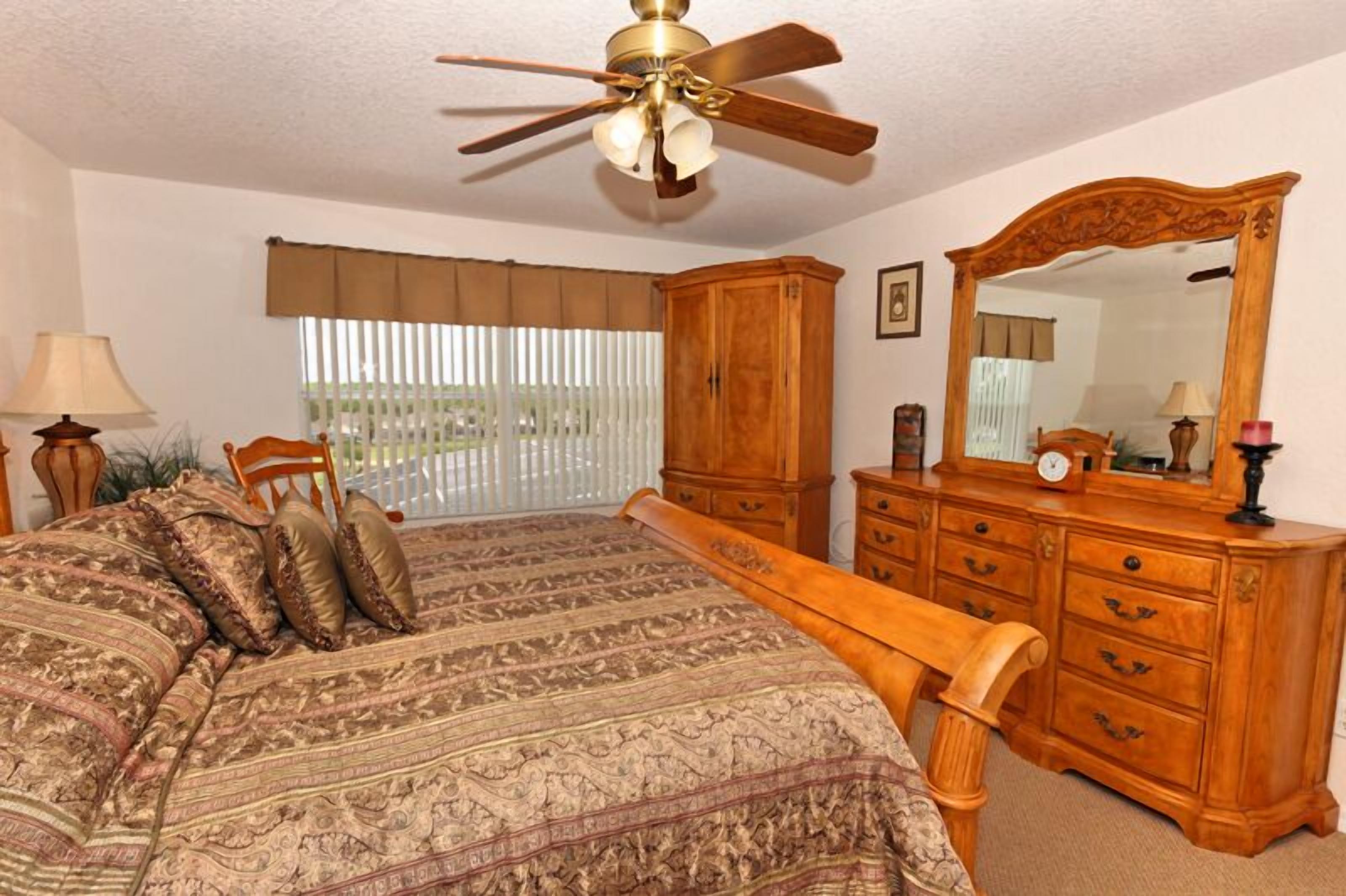 Quarto com cama, cómoda de madeira e ventoinha no teto.