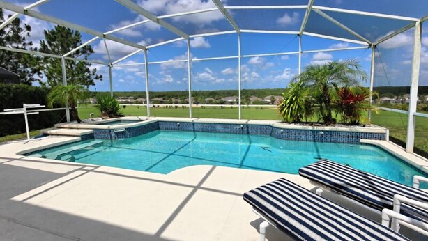 A covered swimming pool with lounge chairs, surrounded by a metal frame and a view of a residential area. - Ov3131 - Highlands Reserve - 5 Bed 3 Baths Villa (Davenport)