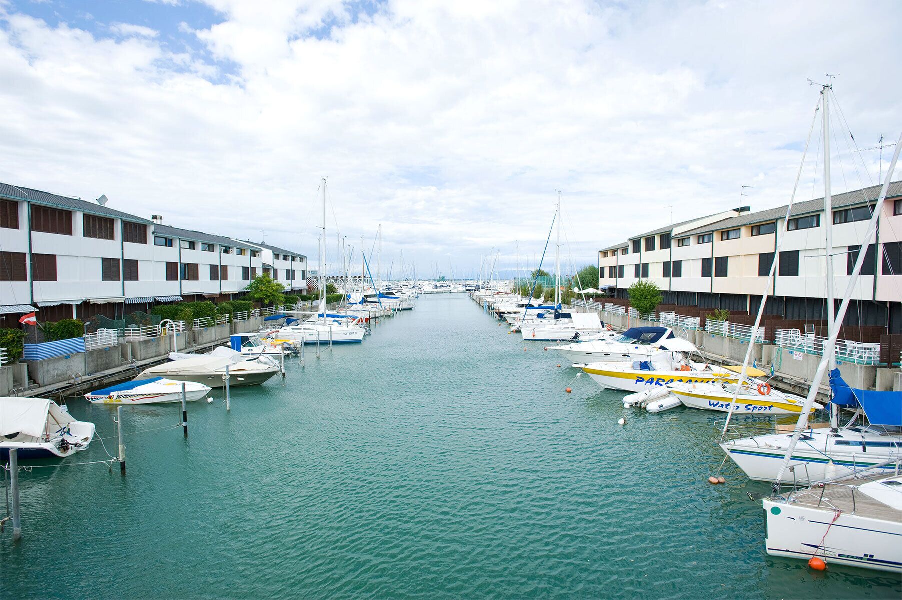 Uma marina com barcos atracados ao longo de um canal, ladeada por edifícios com varandas.