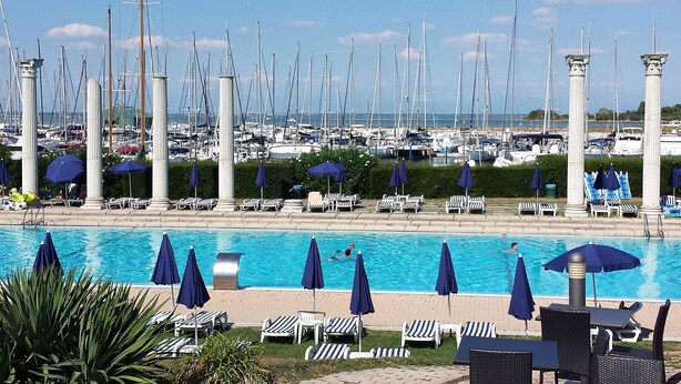 A marina with numerous sailboats, a swimming pool with lounge chairs and umbrellas, and a clear view of the sea. - Isola Terramare (Lignano Sabbiadoro)