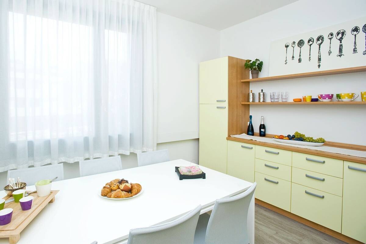 Una cocina moderna con una mesa blanca dispuesta para el desayuno, con cruasanes y tazas de café.